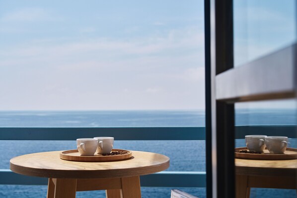 A wooden table with two white cups and a tray of coffee beans, set against a view of the ocean.