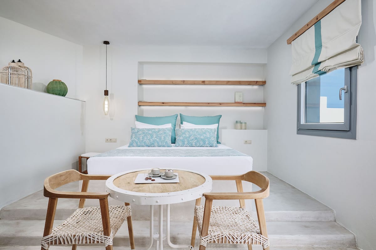 Un dormitorio moderno con una cama, dos sillas, una mesita y un ventanal con cortinas.