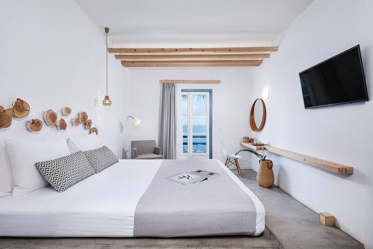 Un dormitorio moderno con una cama grande, un televisor y vista al mar a través de una ventana.