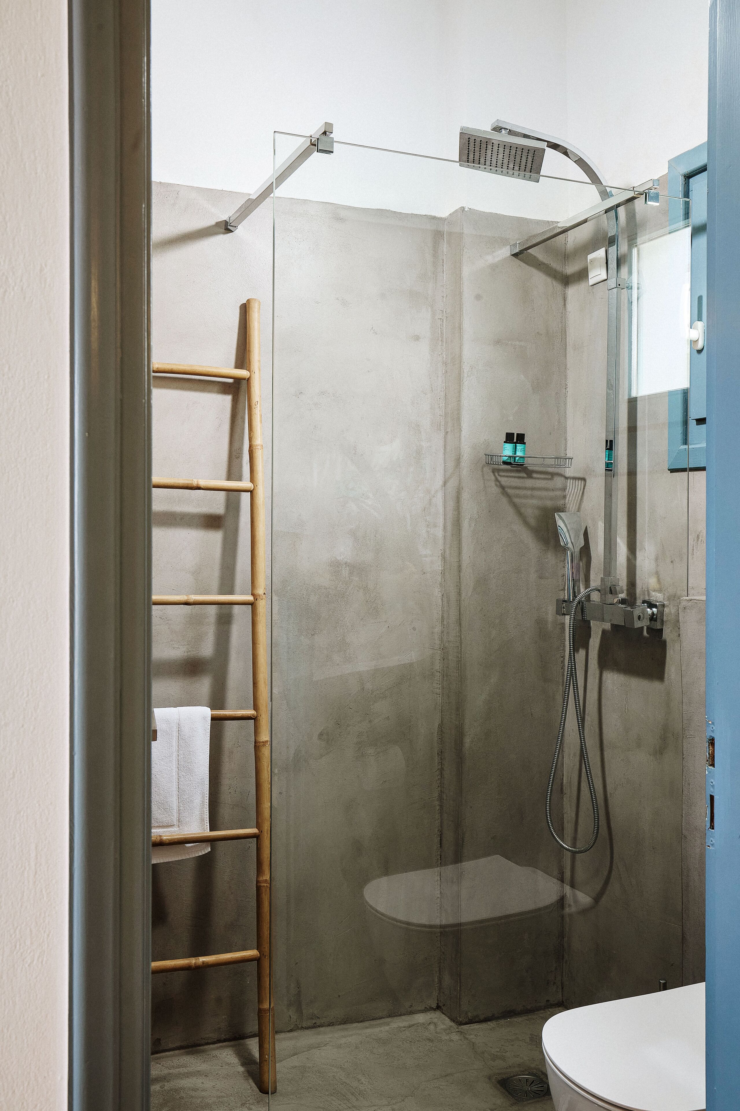 A shower with a glass door, a bamboo ladder, and a white bathtub.