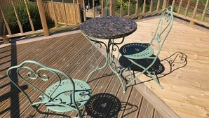 Una terraza de madera con una mesa redonda y dos sillas de metal.