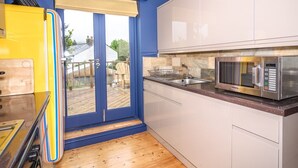 Una cocina moderna con puerta corredera de vidrio que da a una terraza de madera, microondas y armarios blancos.