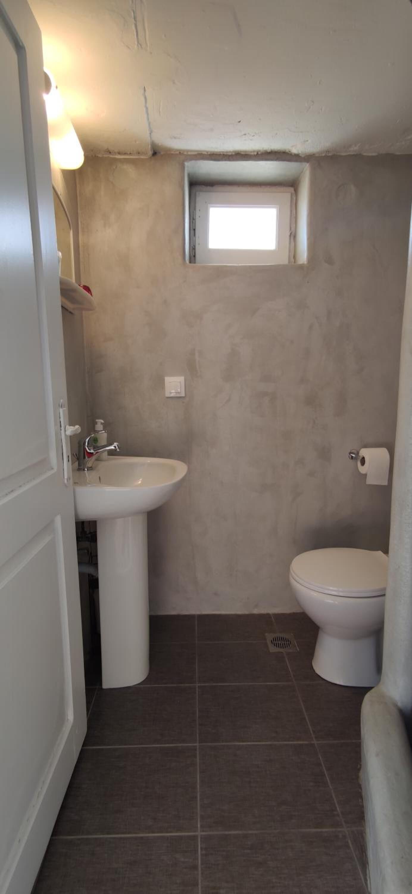 A small bathroom with a white sink, toilet, and a window above the toilet.