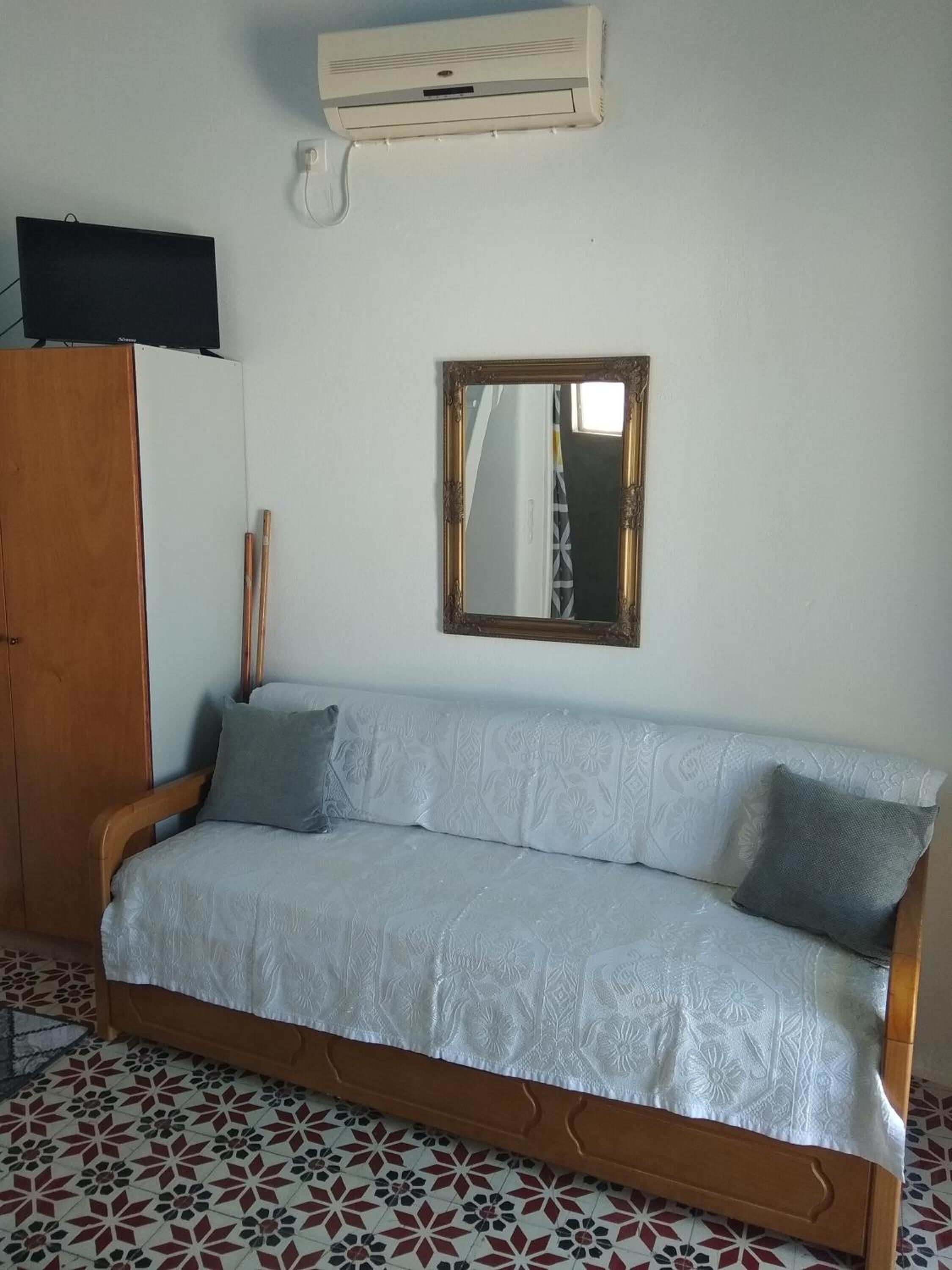 A room with a sofa, a wooden wardrobe, a mirror, and a wall-mounted air conditioner.