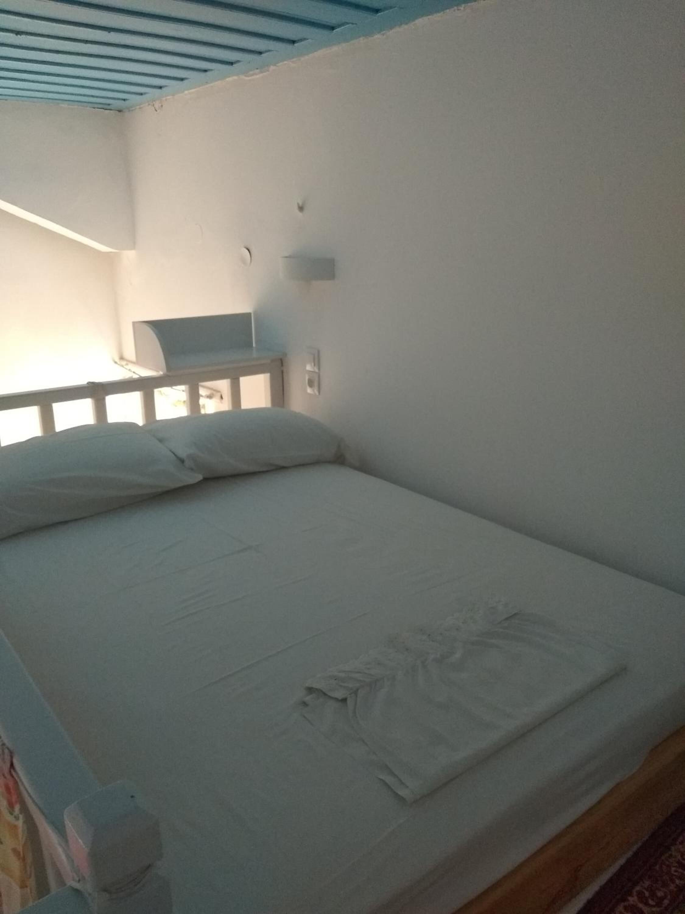 Une chambre avec un lit simple, une tête de lit en bois, une petite table de chevet et un luminaire fixé au mur.