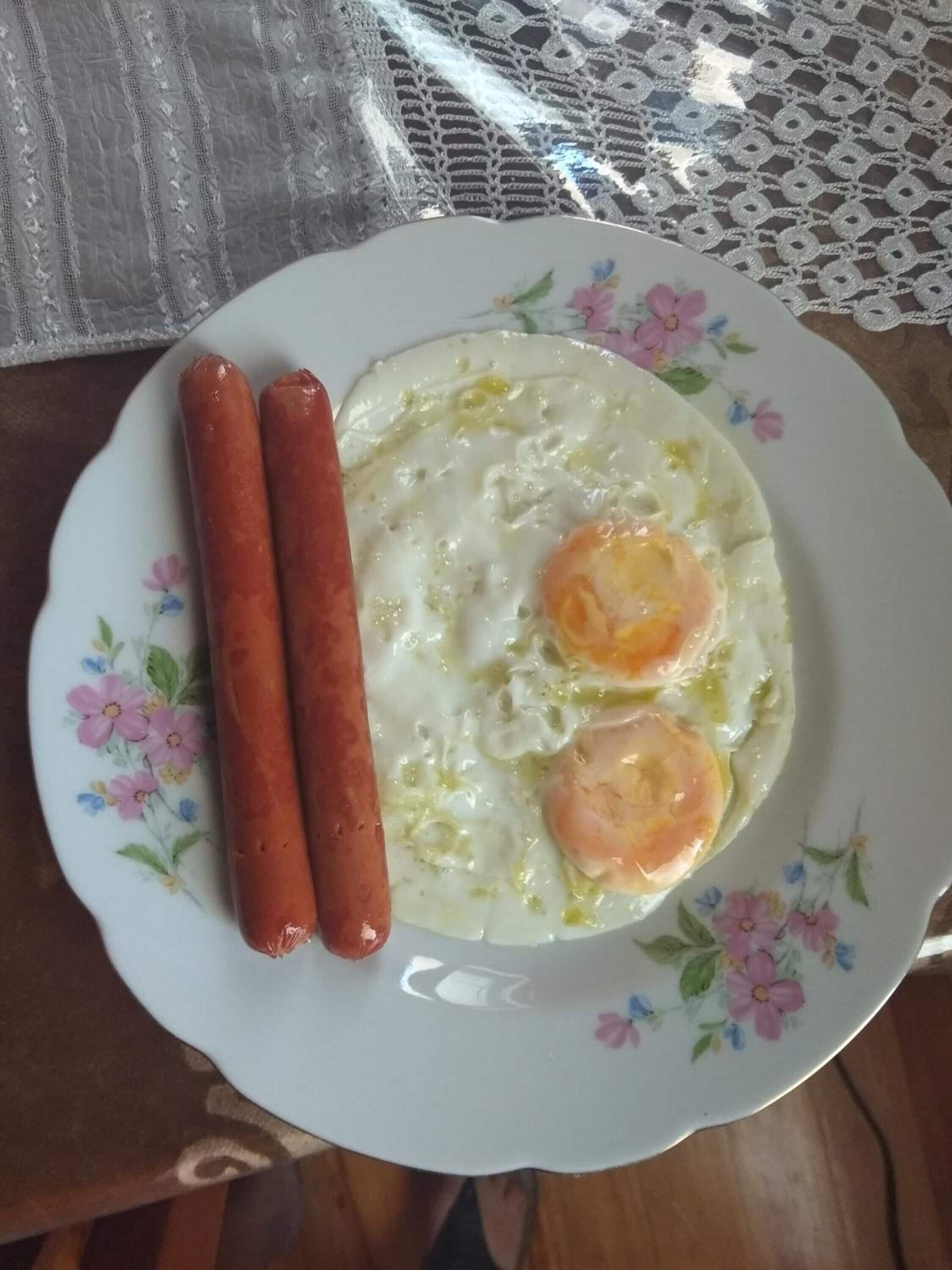 A plate with two sausages and two fried eggs on a floral-patterned plate.