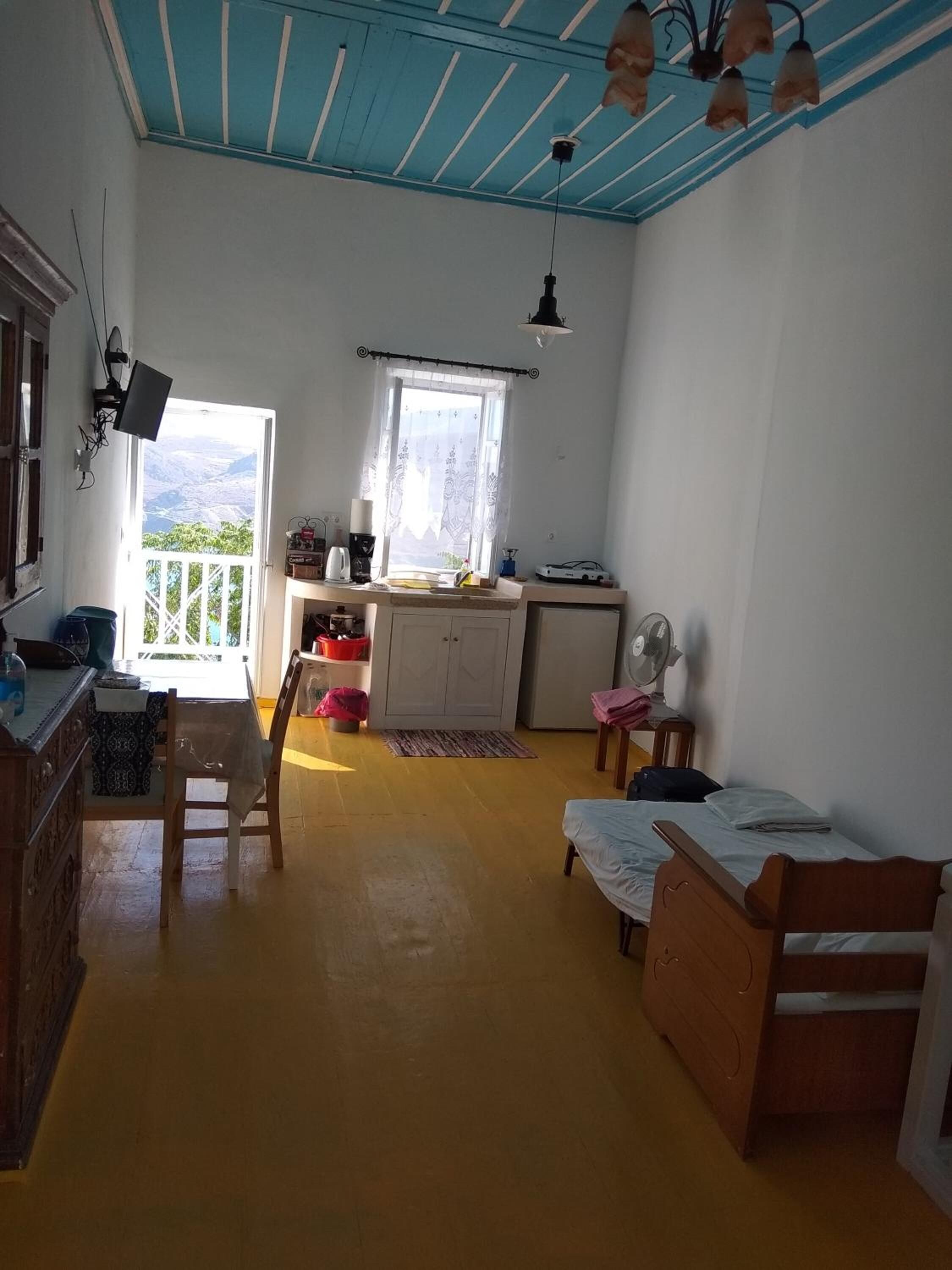 A room with a wooden floor, a bed, a desk, a chair, a window with a view, and a ceiling fan.