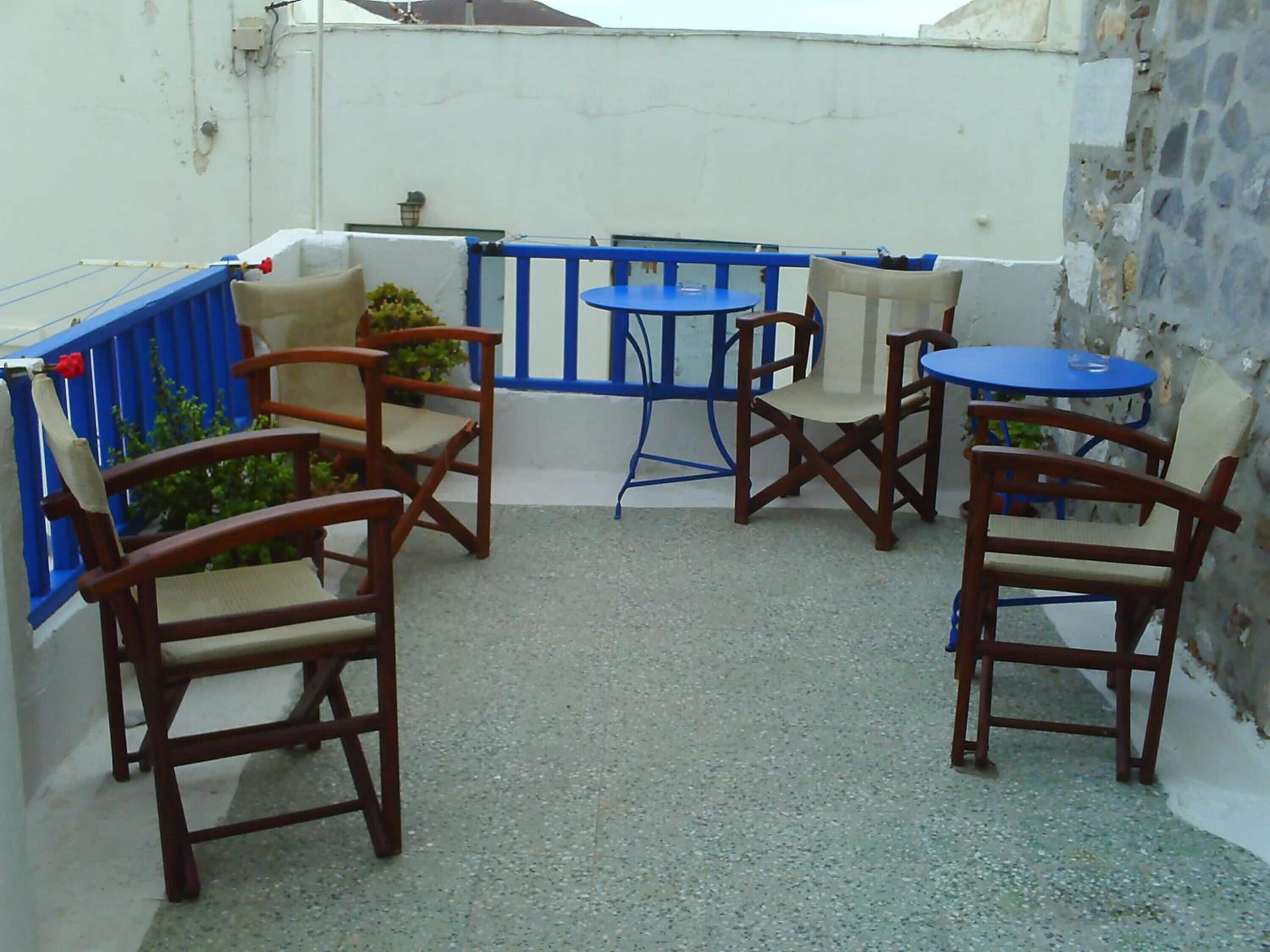 A small outdoor patio with four wooden chairs and two blue tables.