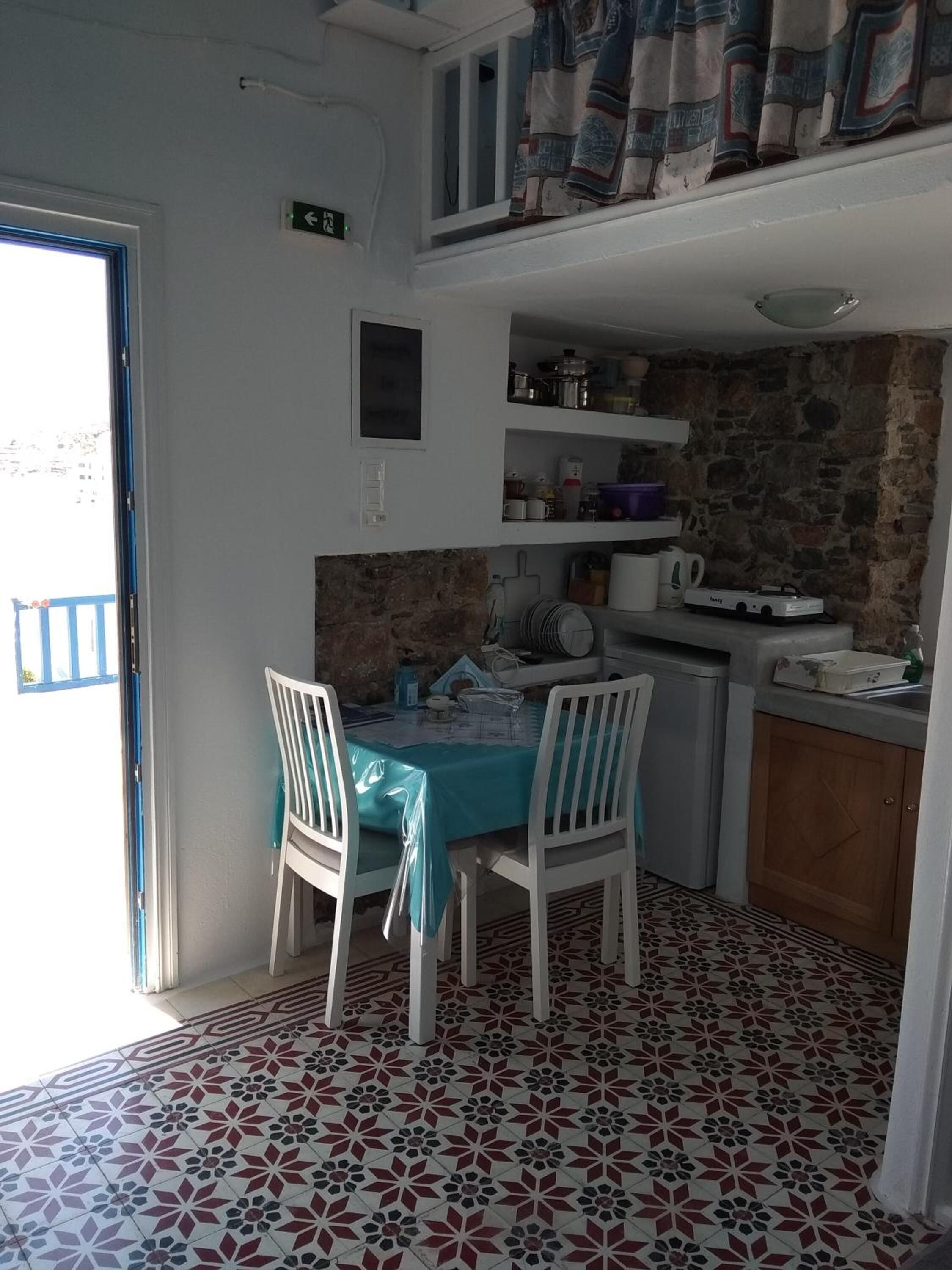 Een compacte keuken met witte kastjes, een betegelde vloer en een eethoek met een tafel en stoelen.