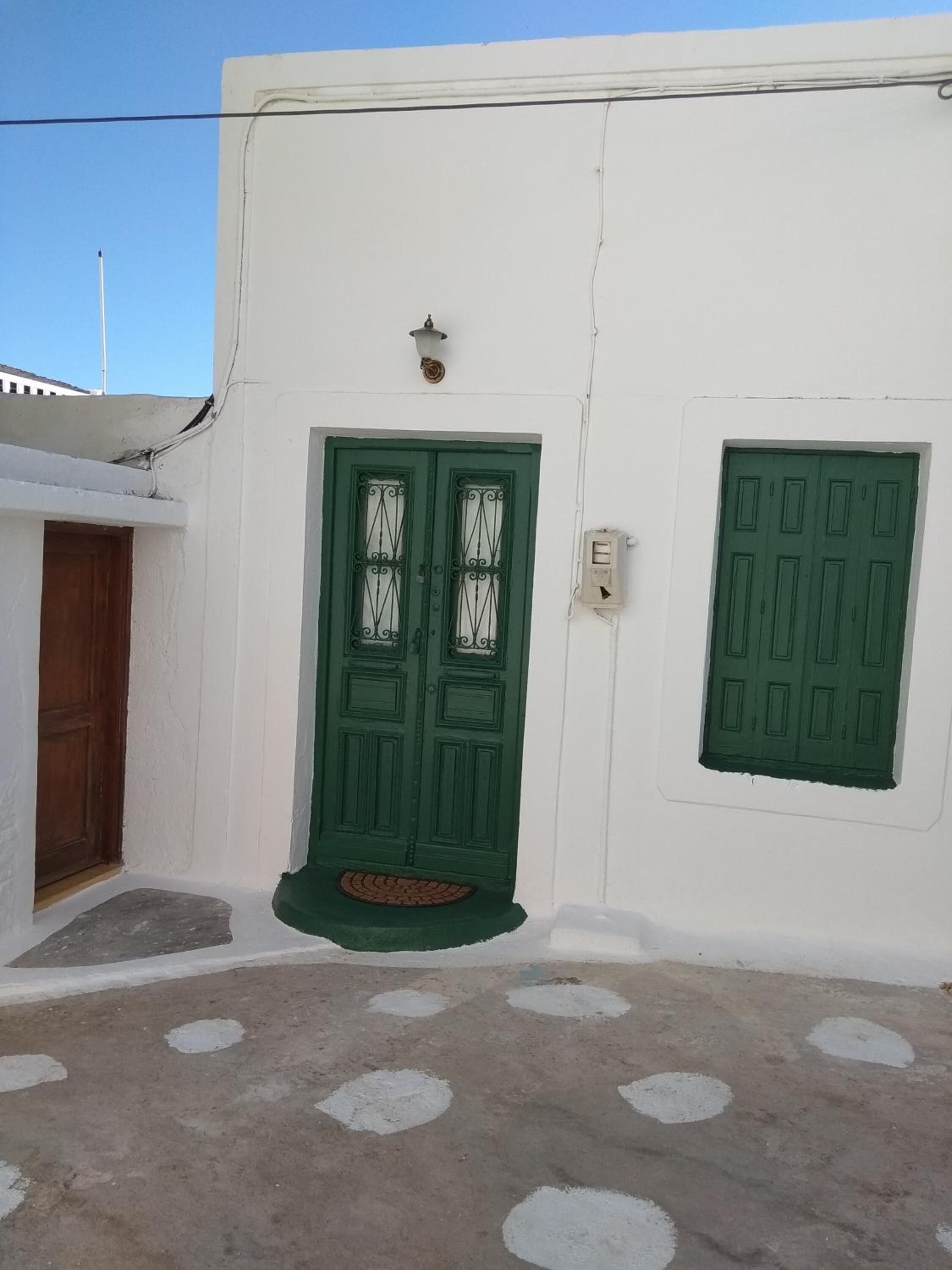 A white building with a green door and window, a small porch, and a concrete ground with circular patterns.