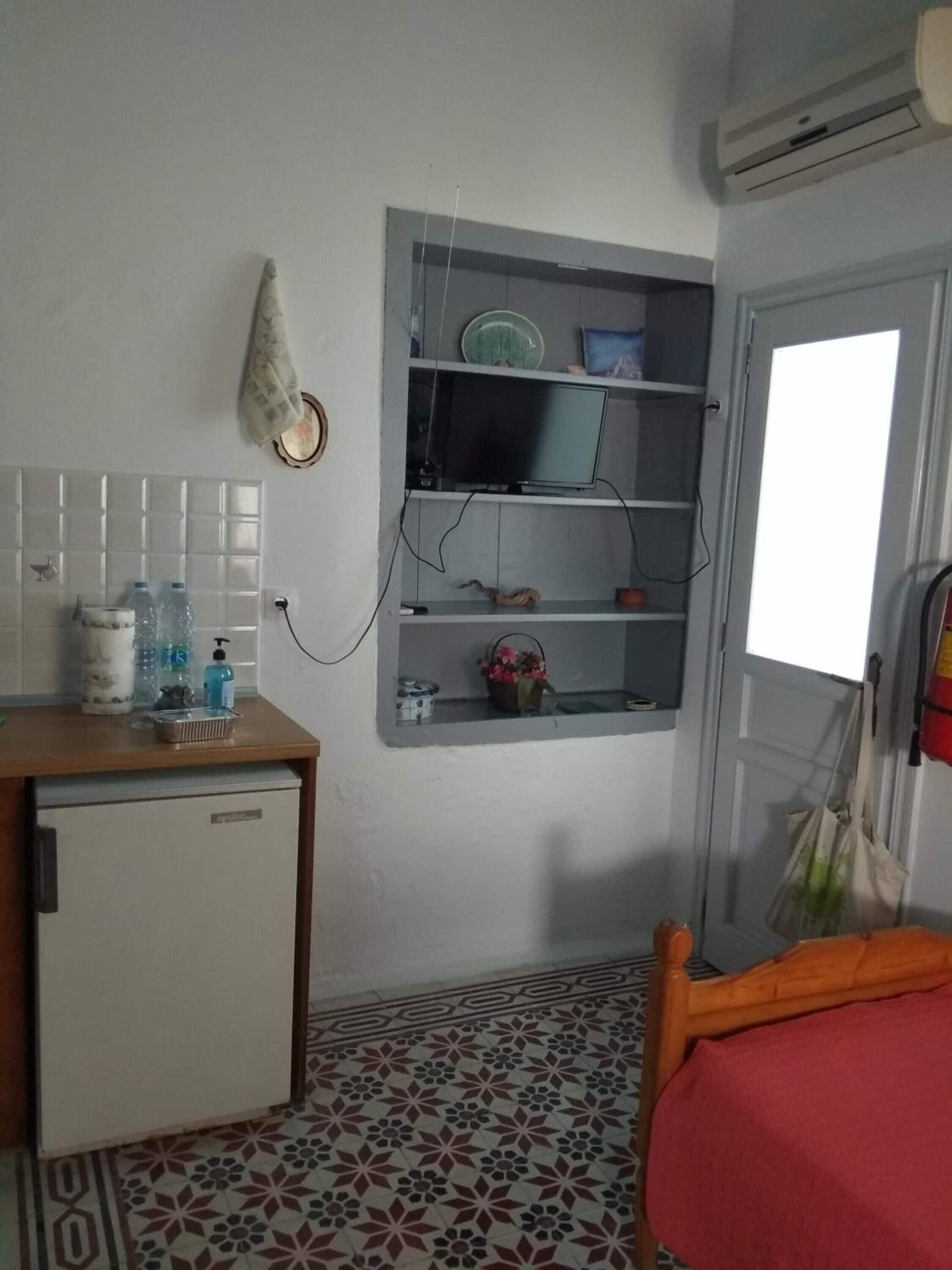 A compact room with a small kitchenette, a bed, a TV mounted on the wall, and a window with a view.