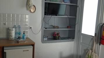 A compact room with a small kitchenette, a bed, a TV mounted on the wall, and a window with a view.