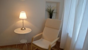 A room with a white chair, a small round table with a lamp, a potted plant, and a white curtain. - Sweet Living Naschmarkt (Vienna)