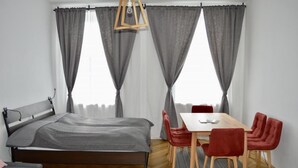 A bedroom with a bed, a dining table with chairs, and a window with curtains. - Sweet Living Naschmarkt (Vienna)