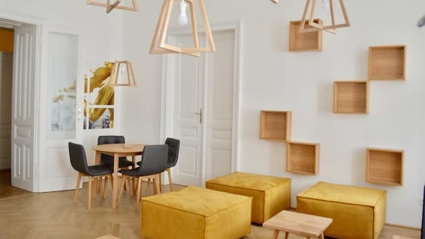 A modern dining area with wooden chairs, a round table, and yellow ottomans. - Sweet Living Naschmarkt (Vienna)