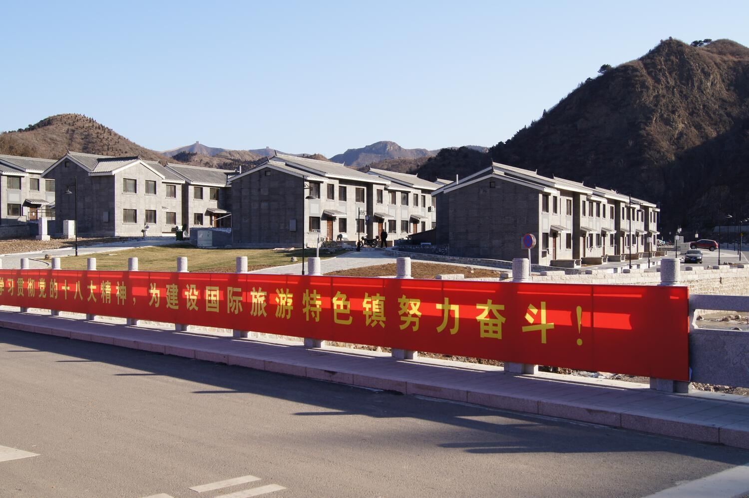 A building with a red barrier in front, a clear sky, and mountains in the background.