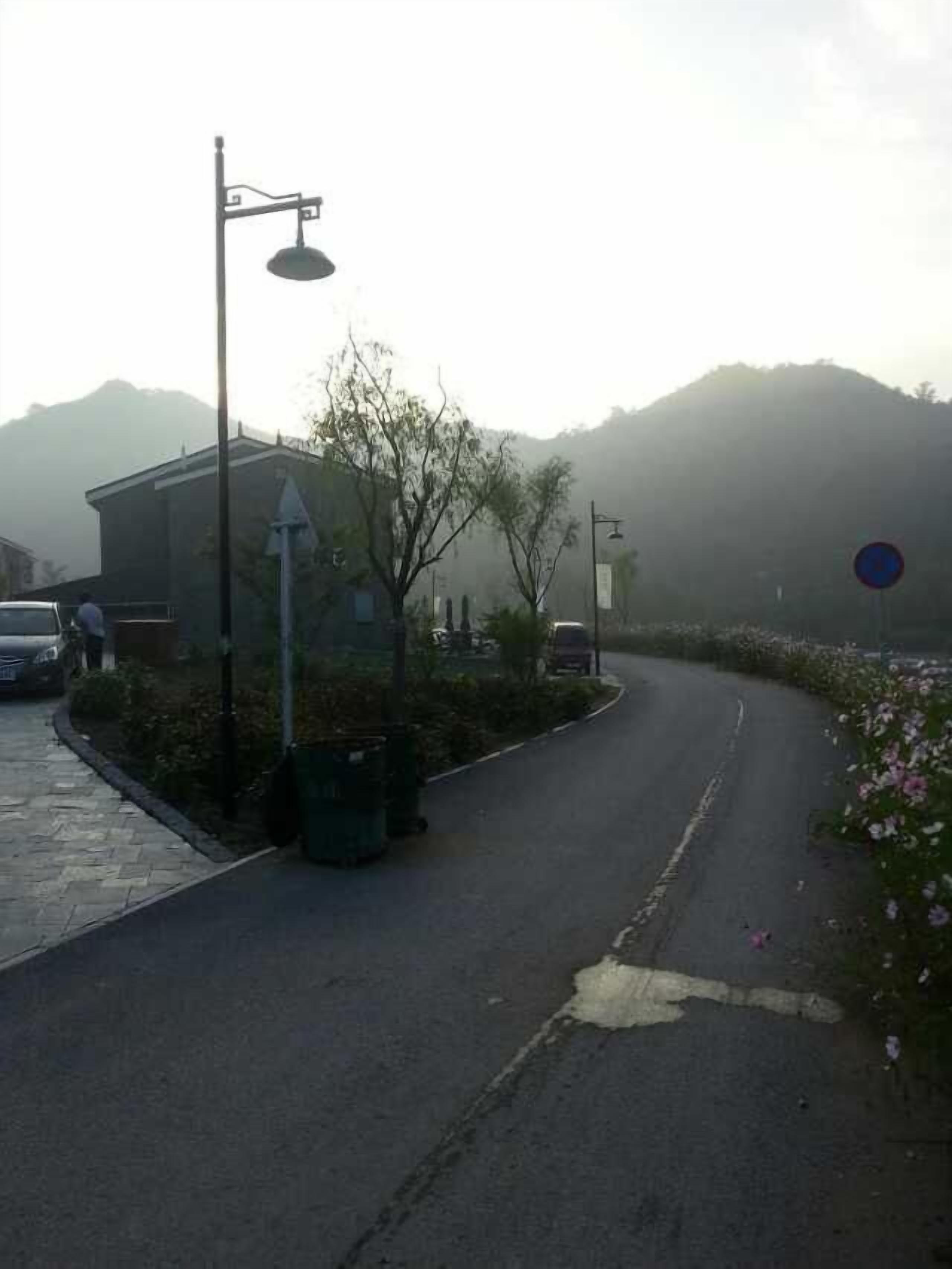 Eine Straße schlängelt sich nach rechts, links ein Gebäude und im Hintergrund ein Berg.