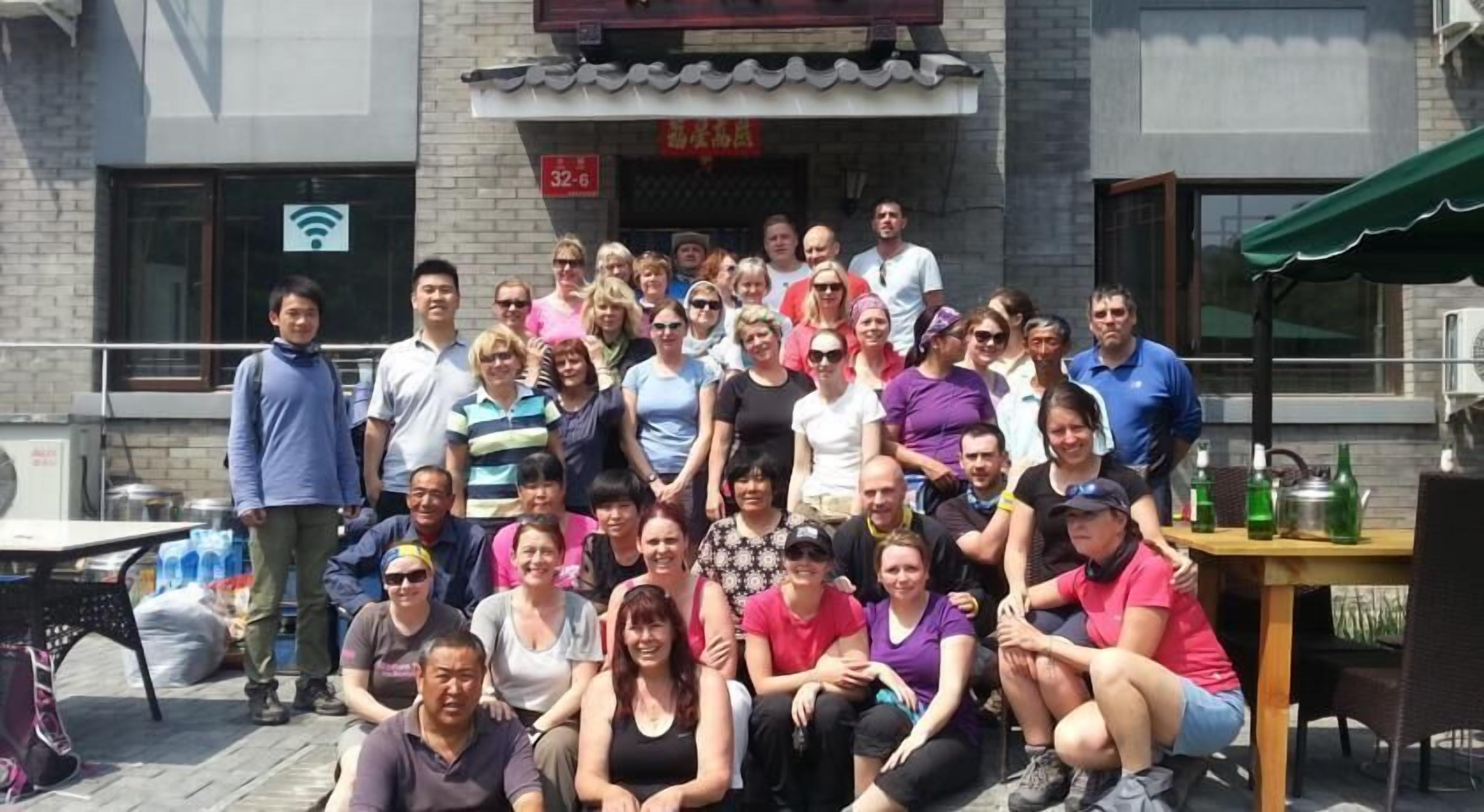 A group of people gathered outside a building with a tiled roof and a sign with numbers.
