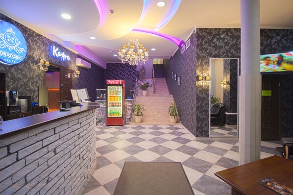 Check-in at our welcoming lobby, featuring a checkered floor, a staircase, and a cozy seating area with potted plants.