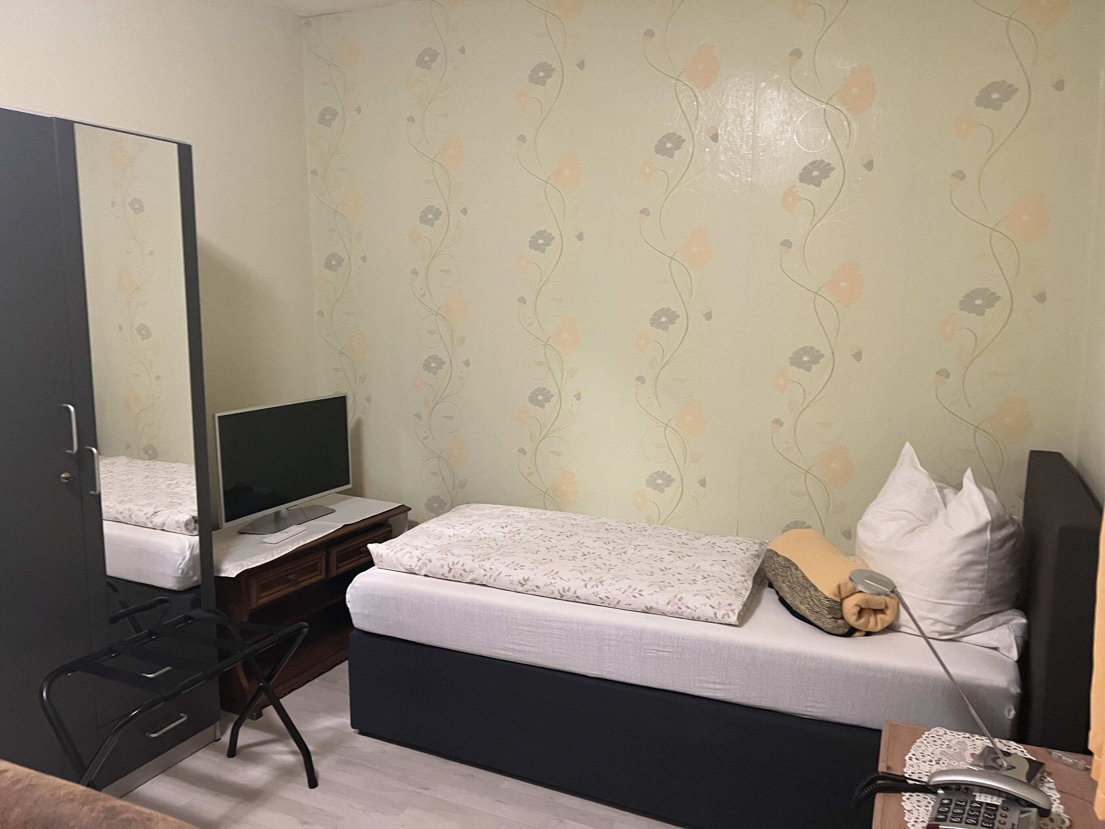 A bedroom with a bed, a desk with a computer, a chair, a mirror, and a telephone.