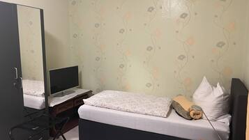 A bedroom with a bed, a desk with a computer, a chair, a mirror, and a telephone.
