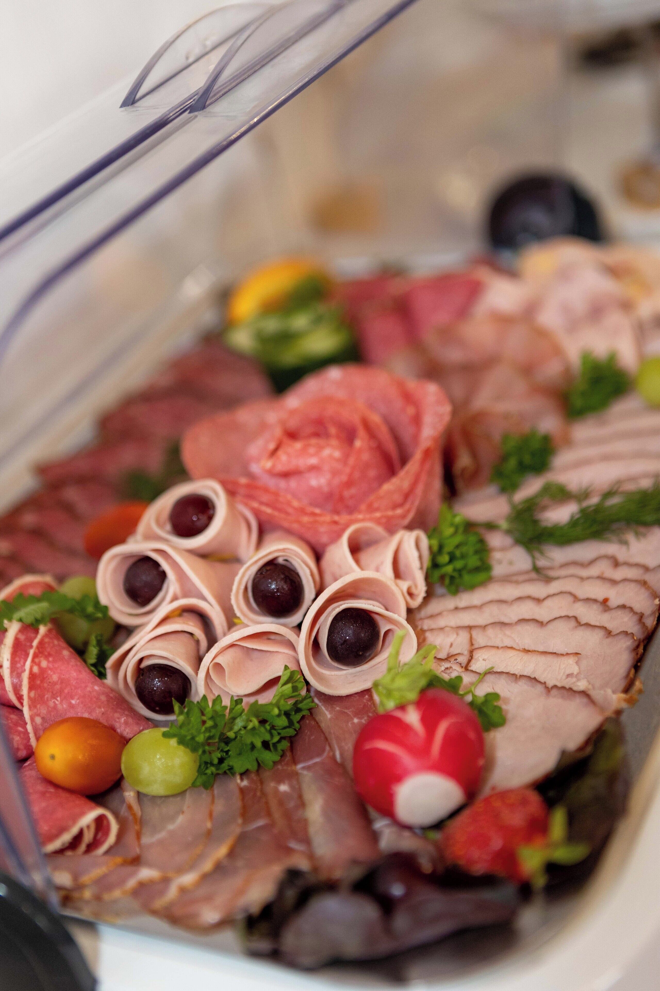 A charcuterie board with various meats, olives, and garnishes.