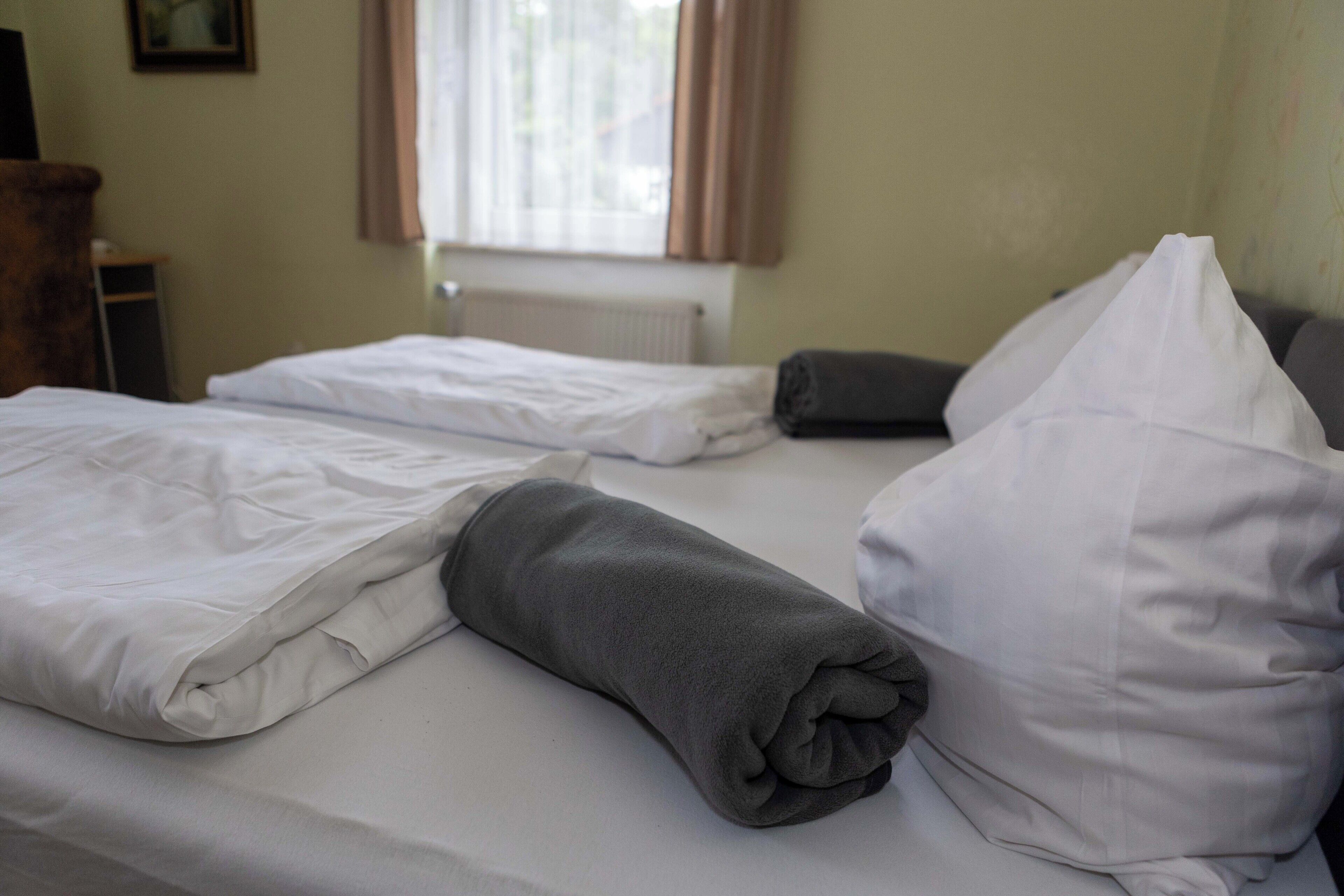 A hotel room with a neatly made bed, a rolled-up blanket, and a pillow.