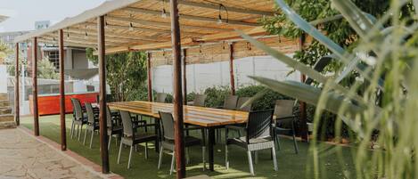 An outdoor patio with a wooden table and chairs, a covered seating area, and a stone pathway.