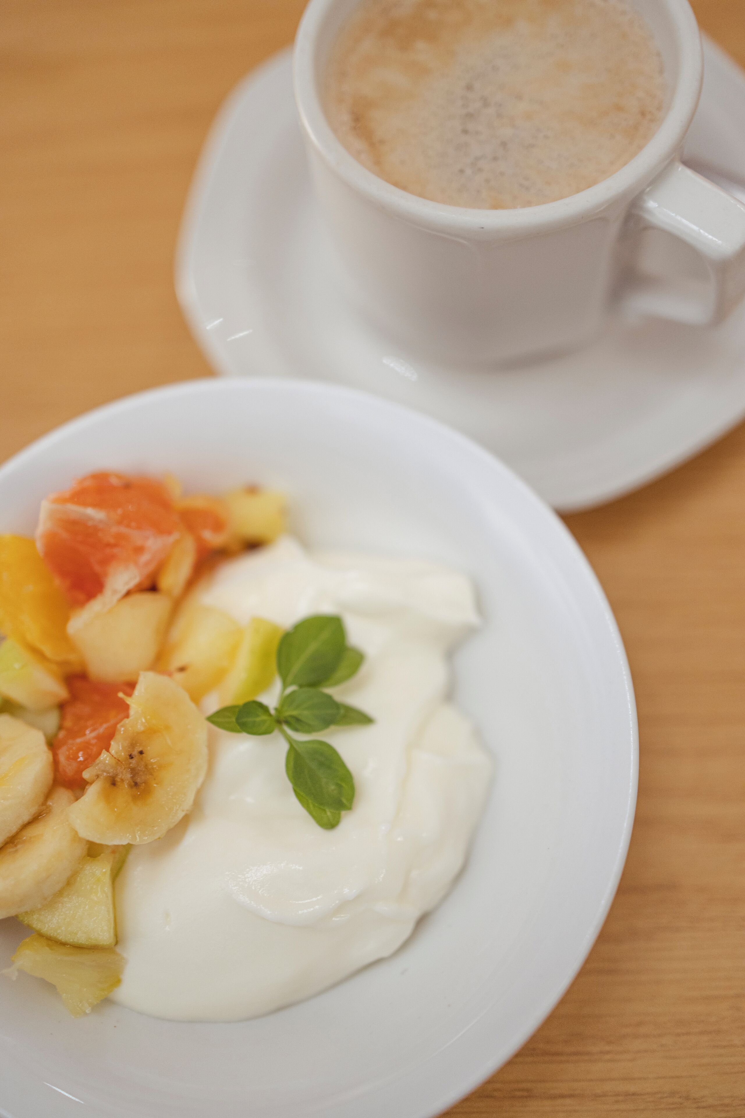 A plate of yogurt with fruit and a cup of coffee on a saucer.