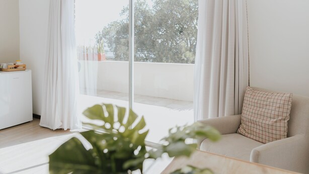 A modern living room with a large window, a sofa, a small side table, and a potted plant. - Hotel Uhland (Windhoek)