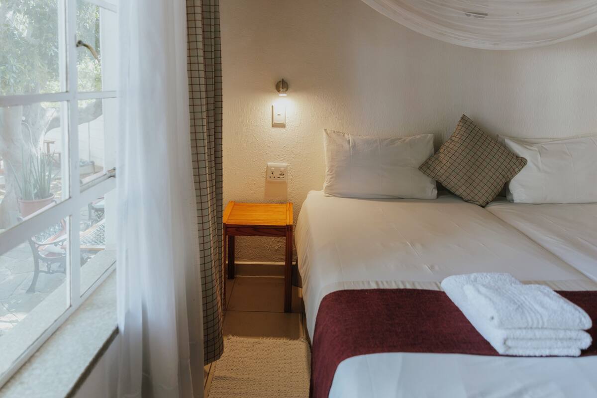 A hotel room with a bed, a nightstand, a lamp, and a window with curtains.