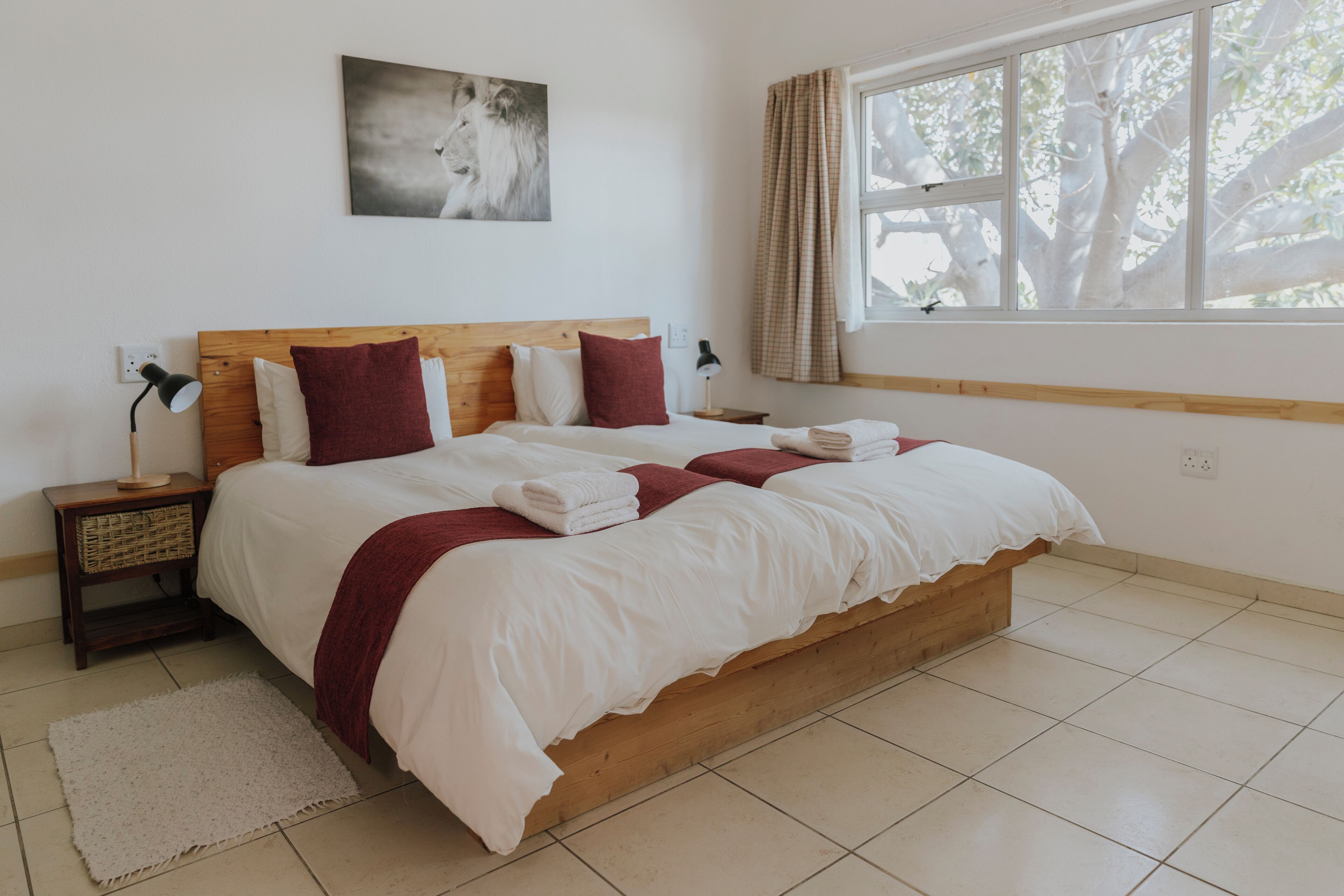 Un lit bien fait, avec du linge de lit blanc et des touches de rouge, une tête de lit en bois et une fenêtre avec des rideaux.