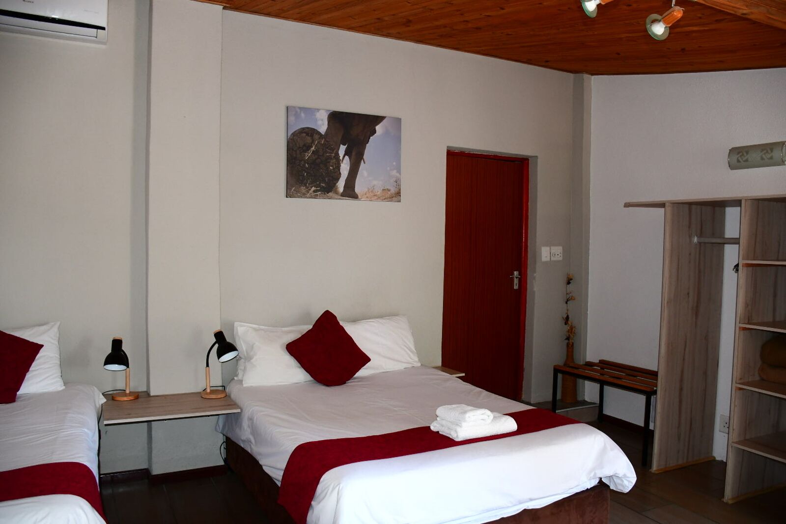 A hotel room with a bed, a nightstand, a red door, and a wooden wardrobe.