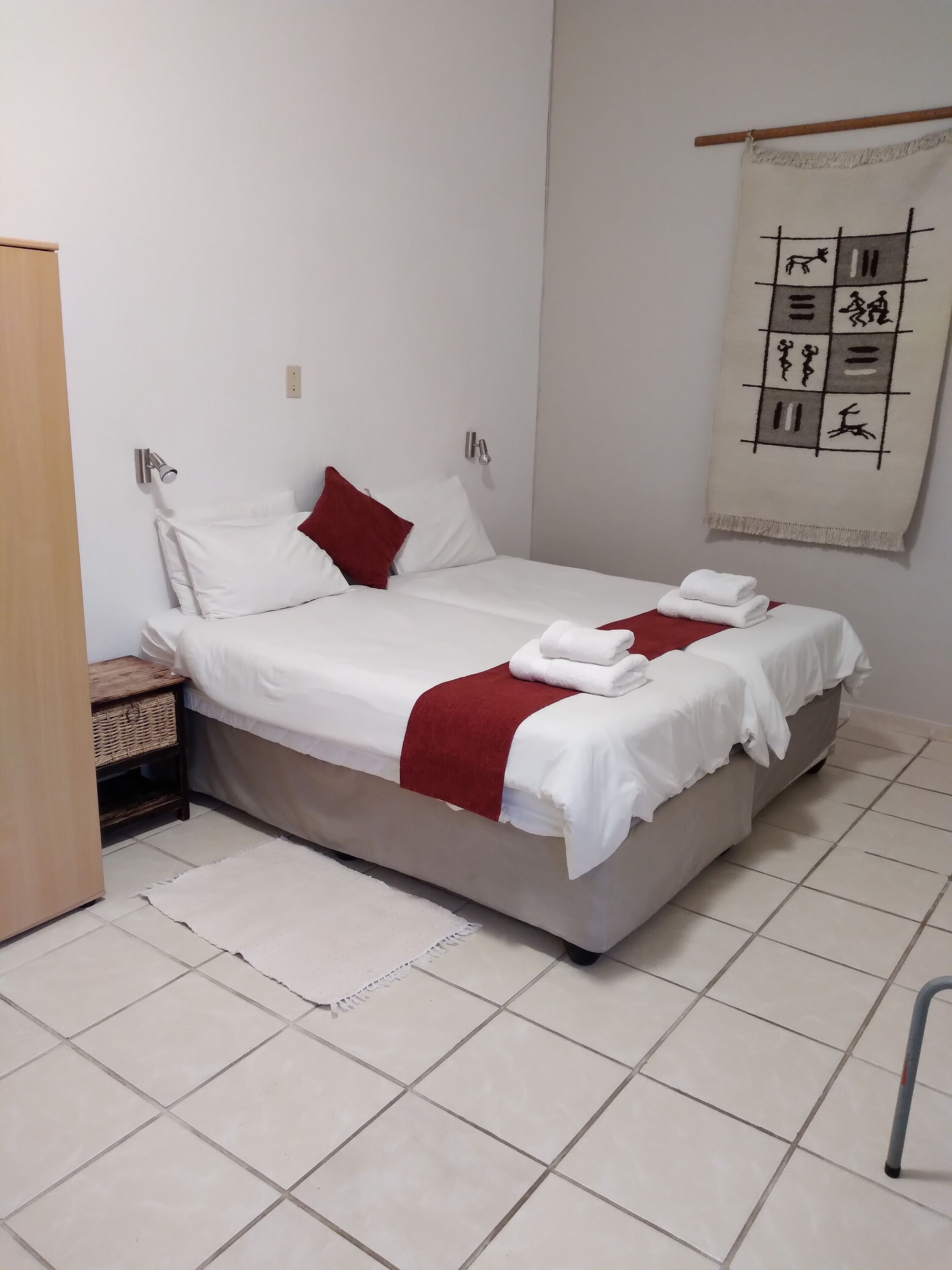 A neatly made bed with white and red bedding, a wooden nightstand, and a wall-mounted light fixture.