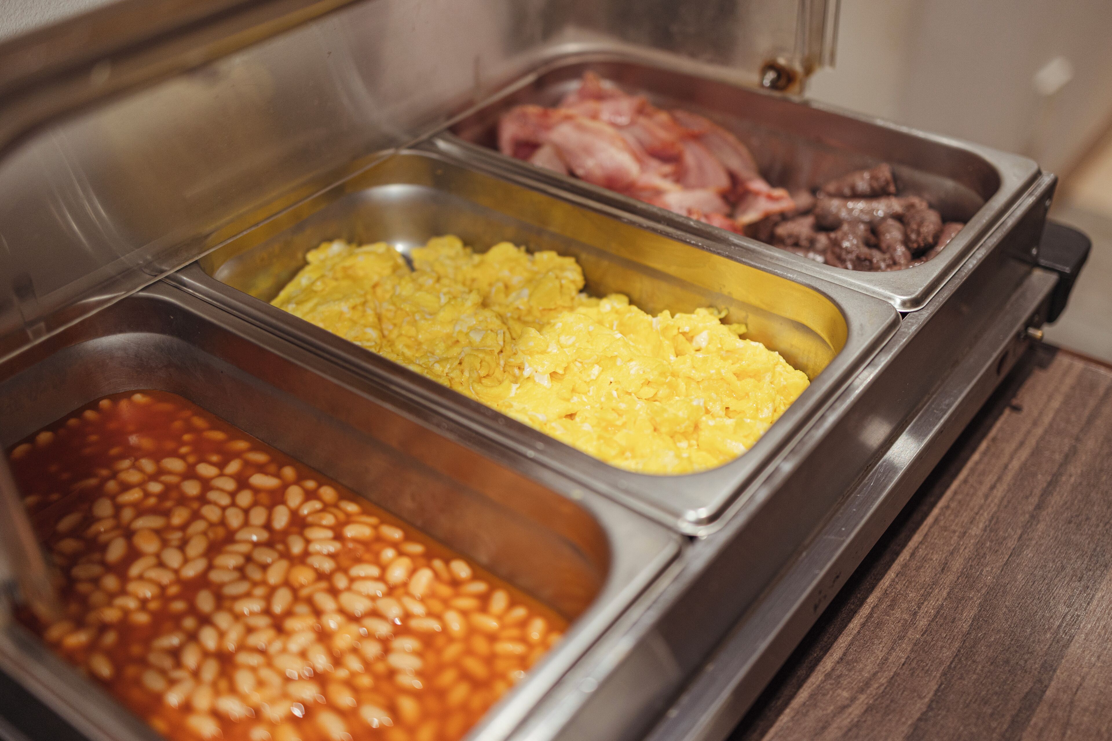 A buffet with various food options including beans, scrambled eggs, and meat.