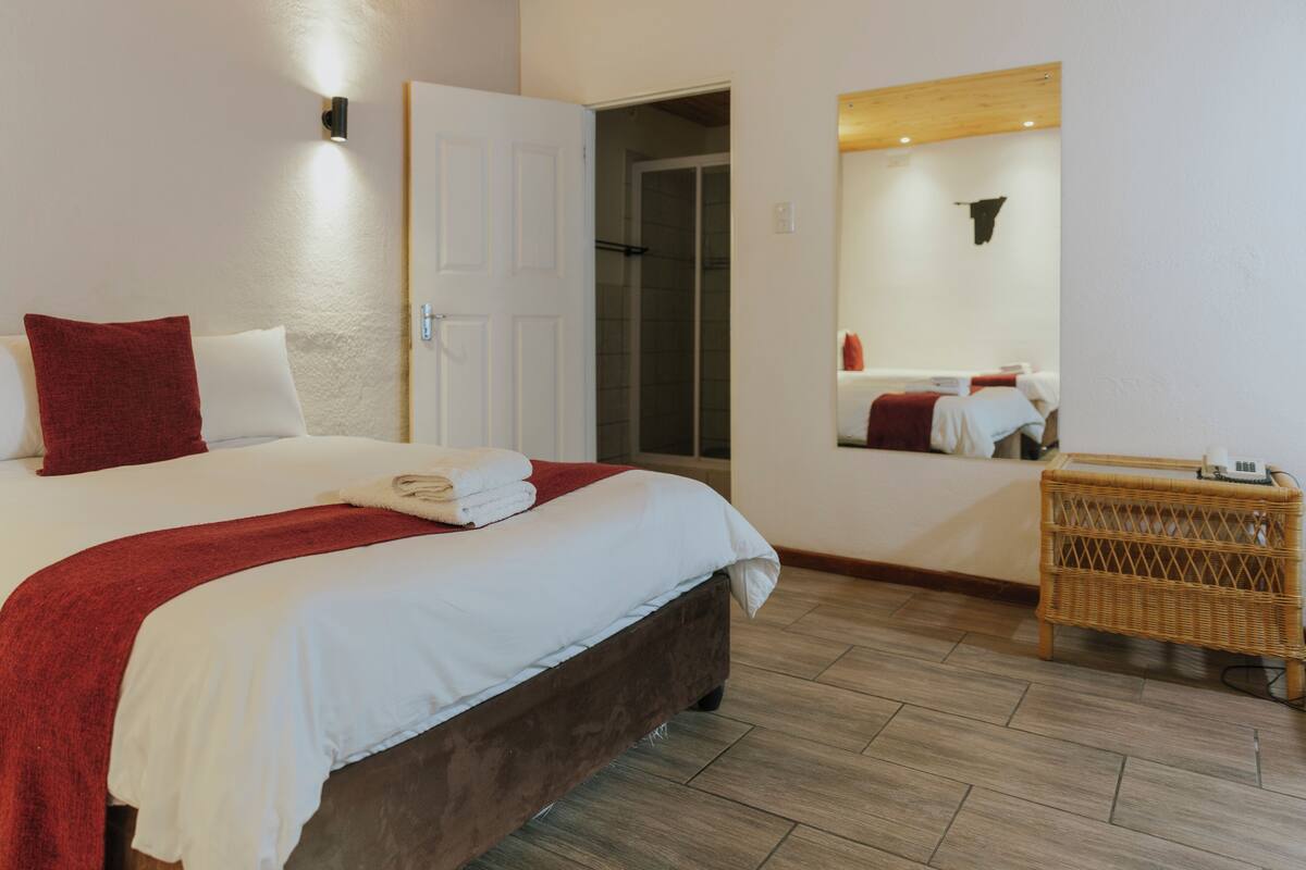 A hotel room with a bed, a door, a mirror, and a wicker side table.