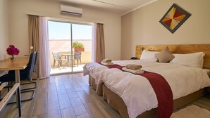 A hotel room with a bed, a desk, a chair, a small table, and a balcony with a chair and potted plant. - Hotel Uhland (Windhoek)