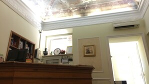 A room with a high ceiling, a wooden desk, a clock, and a framed picture on the wall. - Hotel Positano (Rome)