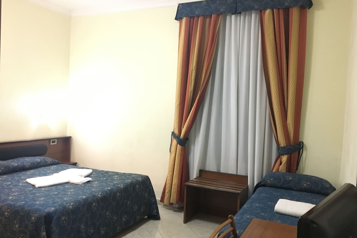 Quarto de hotel com duas camas, um pequeno banco de madeira e uma escrivaninha.