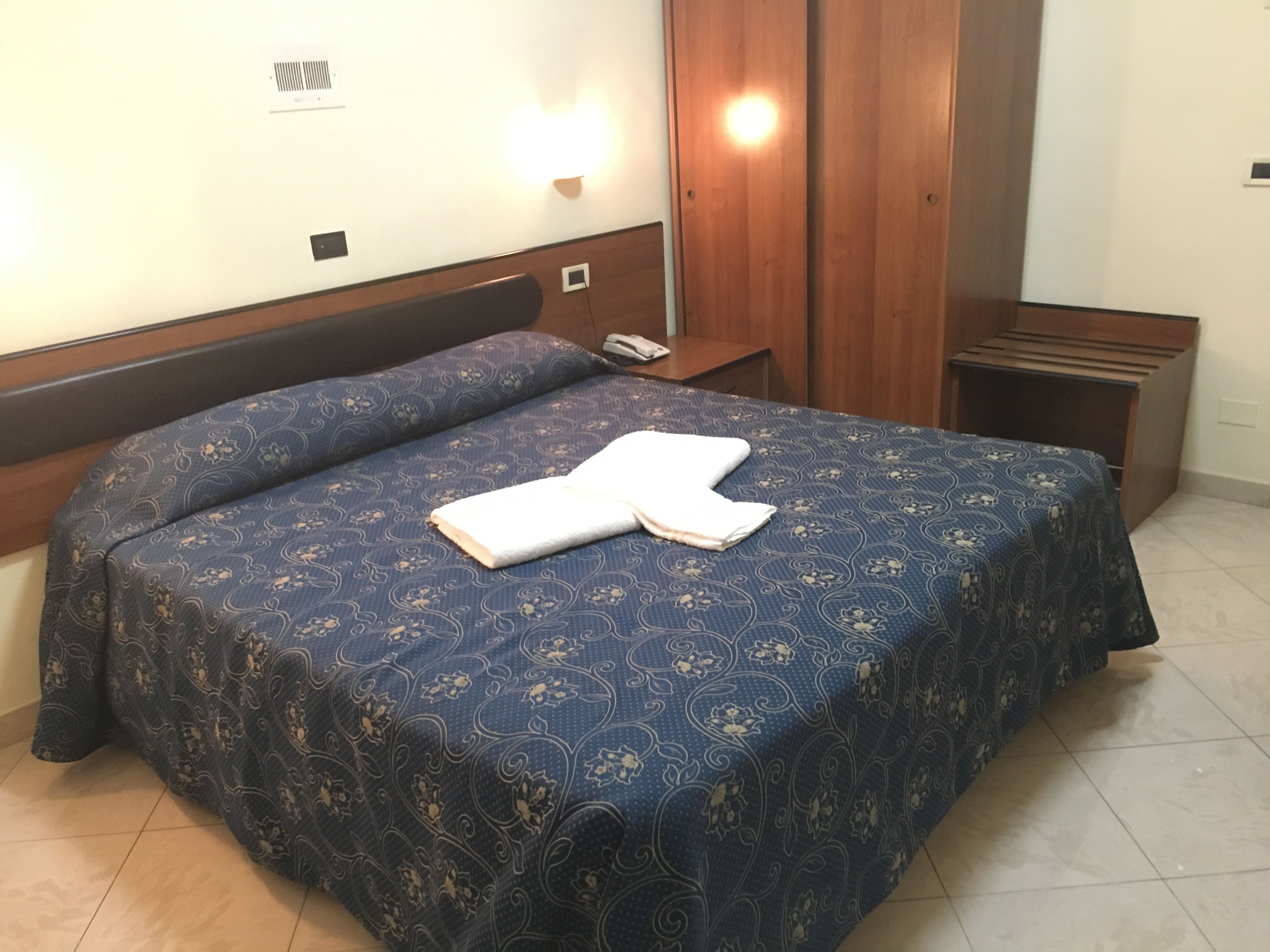 Une chambre d’hôtel avec un lit double, une table de chevet avec une lampe et une armoire en bois.