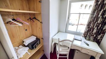 Habitació compacta amb un armari de fusta, un escriptori blanc, una cadira i una finestra amb cortines.