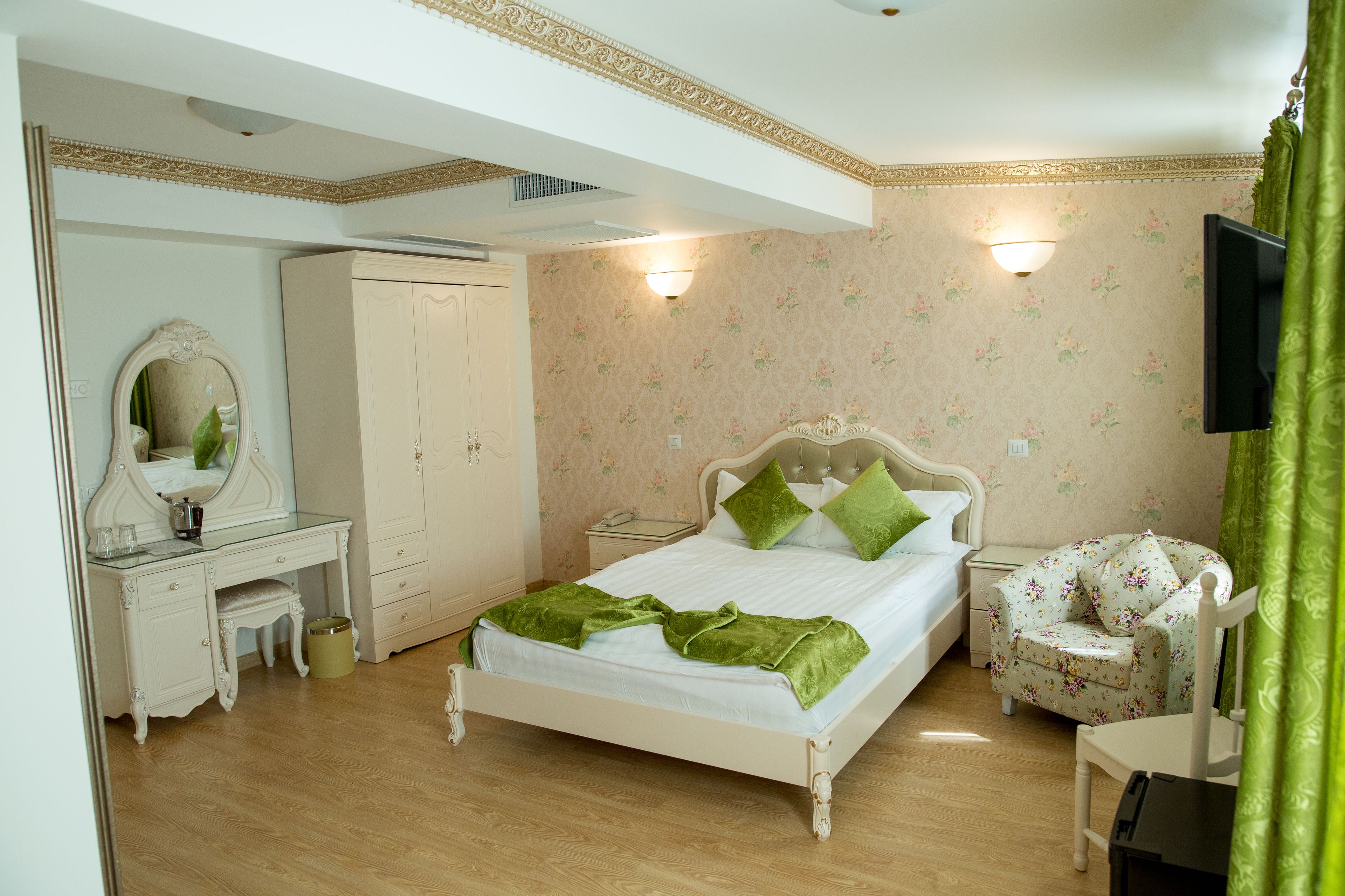 A bedroom with a bed, a dresser, a vanity, a chair, and a television.