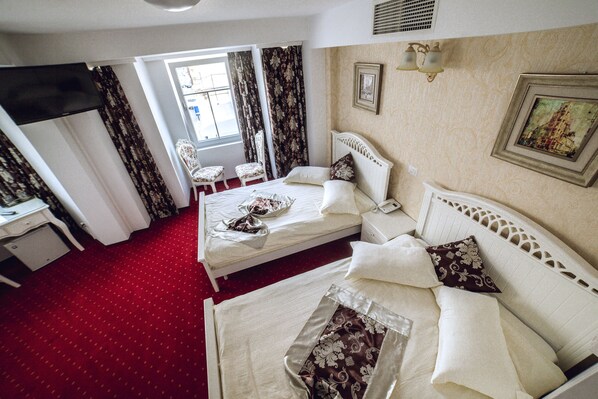 A hotel room with two beds, a desk, a chair, and a window with curtains. - Hotel Helin Central (Craiova)