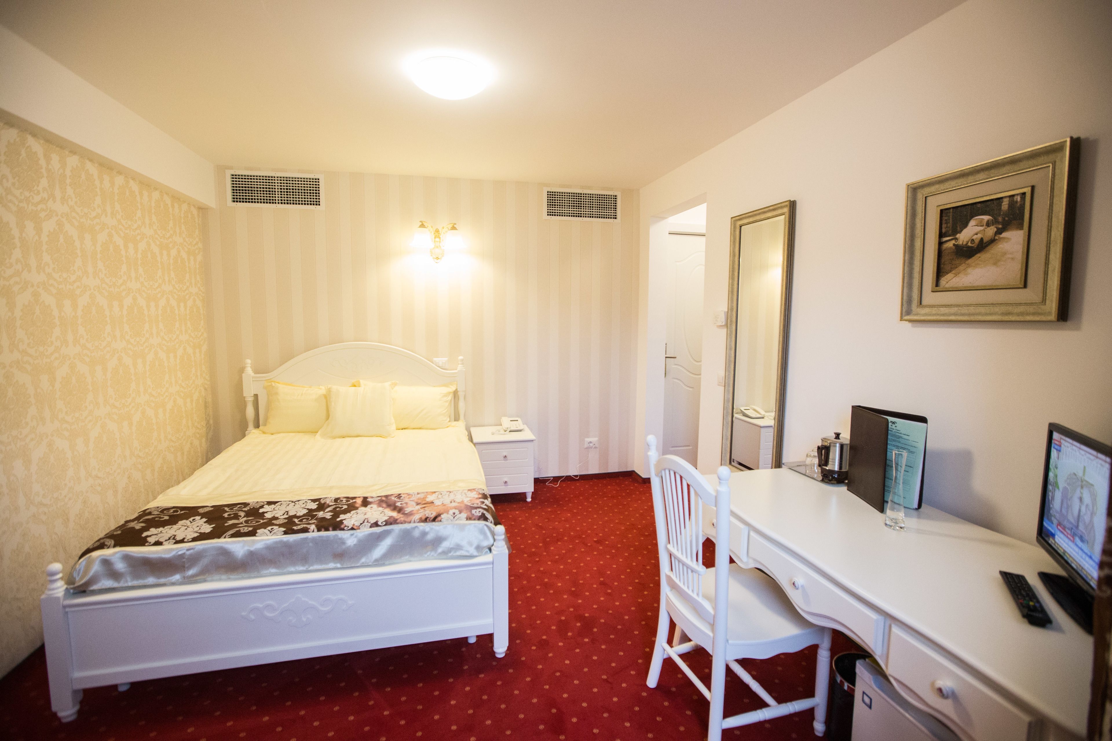 Una habitación de hotel con cama, mesita de noche, escritorio, silla y un espejo grande.