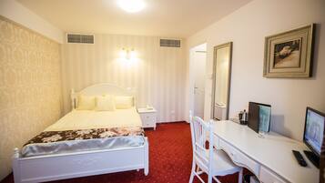 Una habitación de hotel con cama, mesita de noche, escritorio, silla y un espejo grande.
