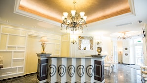 A reception area with a marble floor, a central counter with a decorative design, a chandelier, and a large mirror above the counter. - Hotel Helin Central (Craiova)
