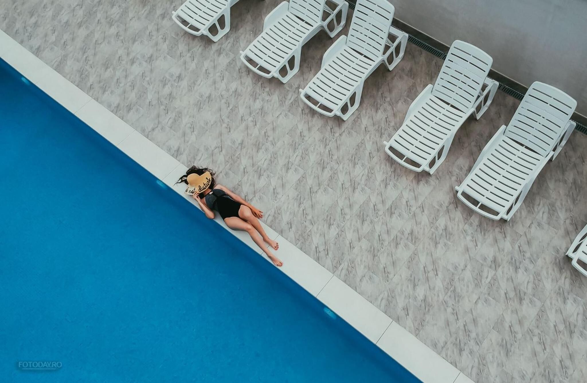 A swimming pool with white lounge chairs arranged along the edge.