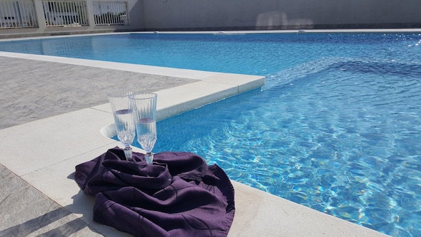 A swimming pool with clear blue water, two glasses of water, and a purple towel on the edge. - Vila Kharisma (Navodari)