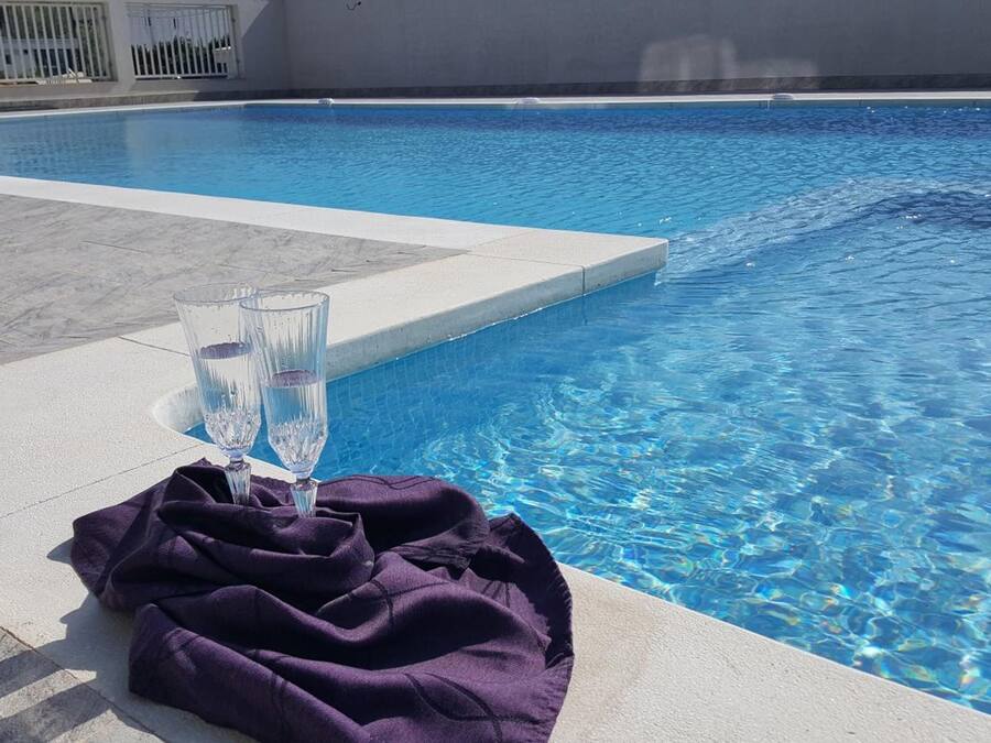 Una piscina con agua azul cristalina, dos vasos de agua y una toalla morada en el borde.