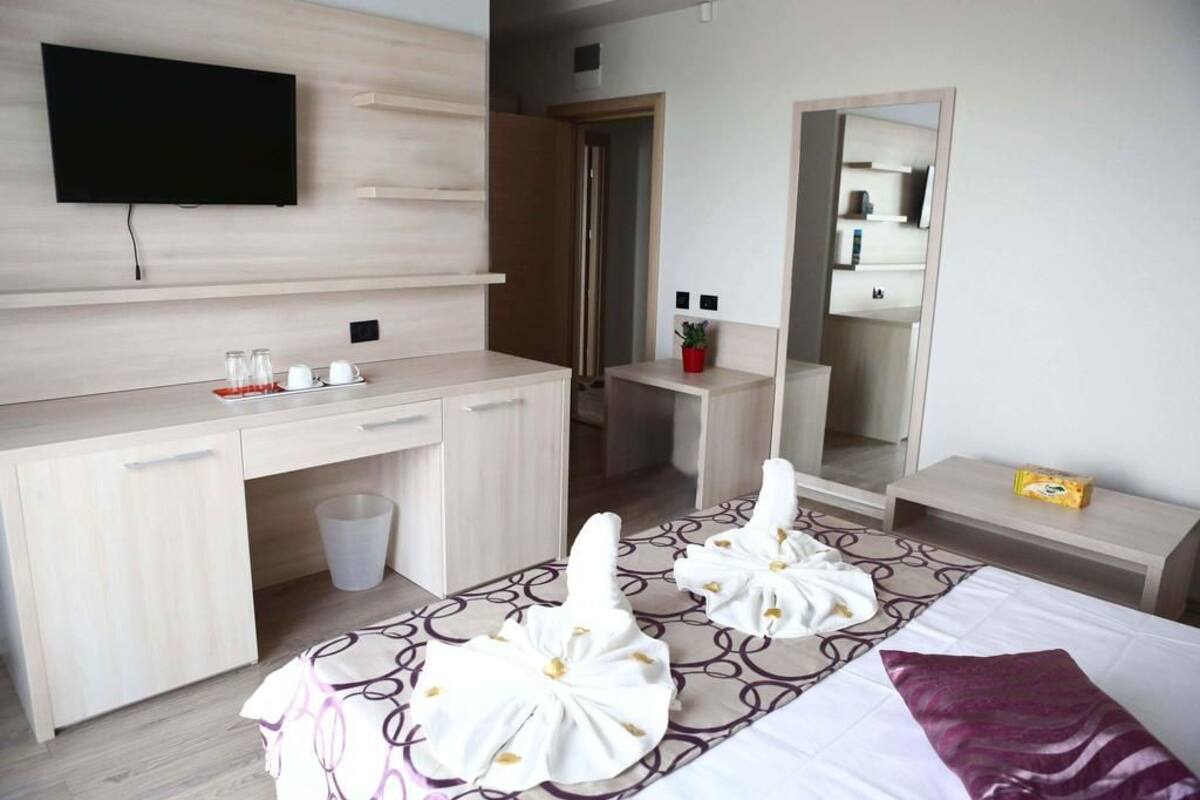 A hotel room with a bed, a desk, a TV mounted on the wall, a mirror, and a bathroom visible through an open door.